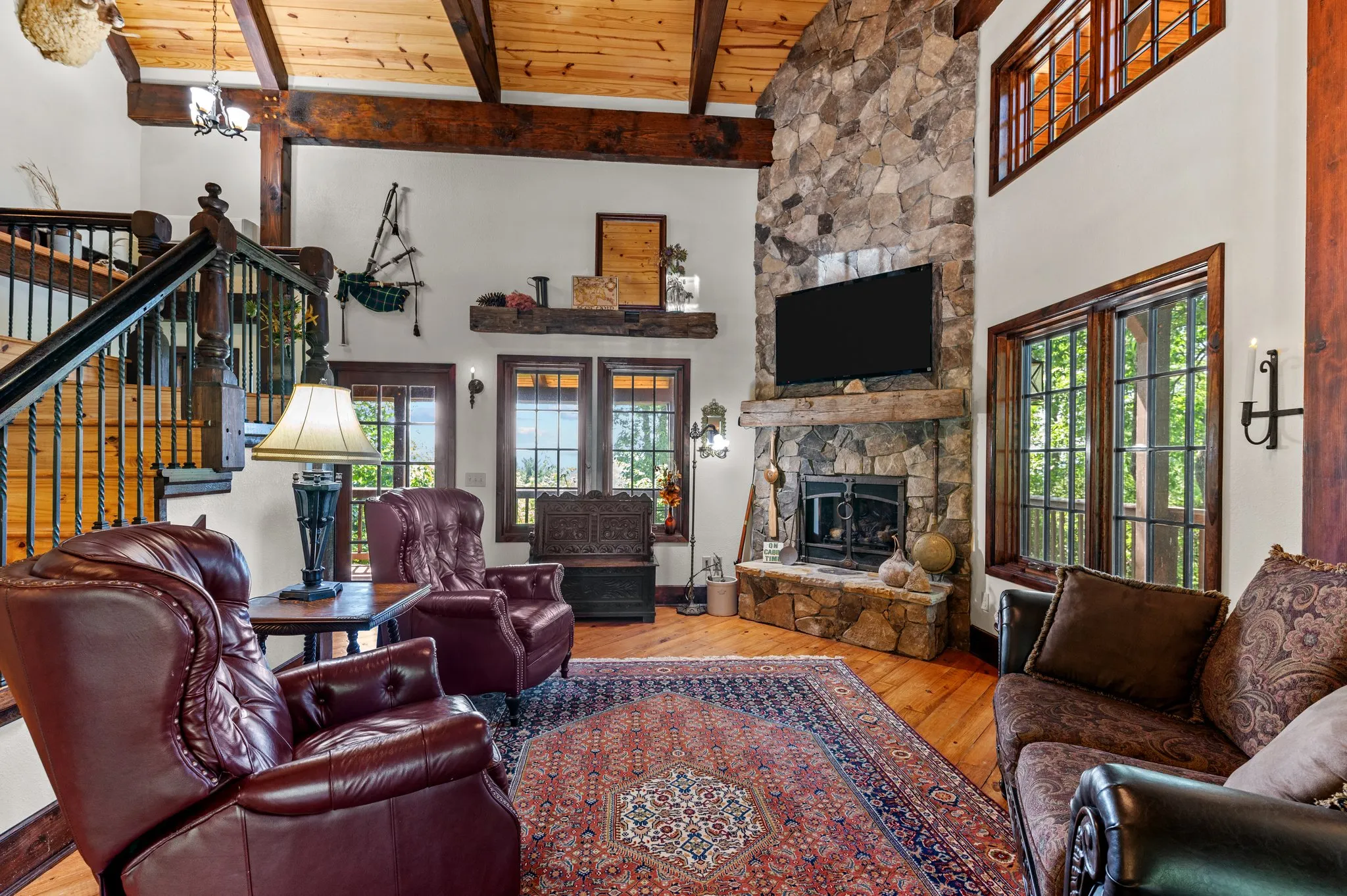 Living area featuring burgundy leather chairs, ornate fireplace, exposed wood beams and glass doors