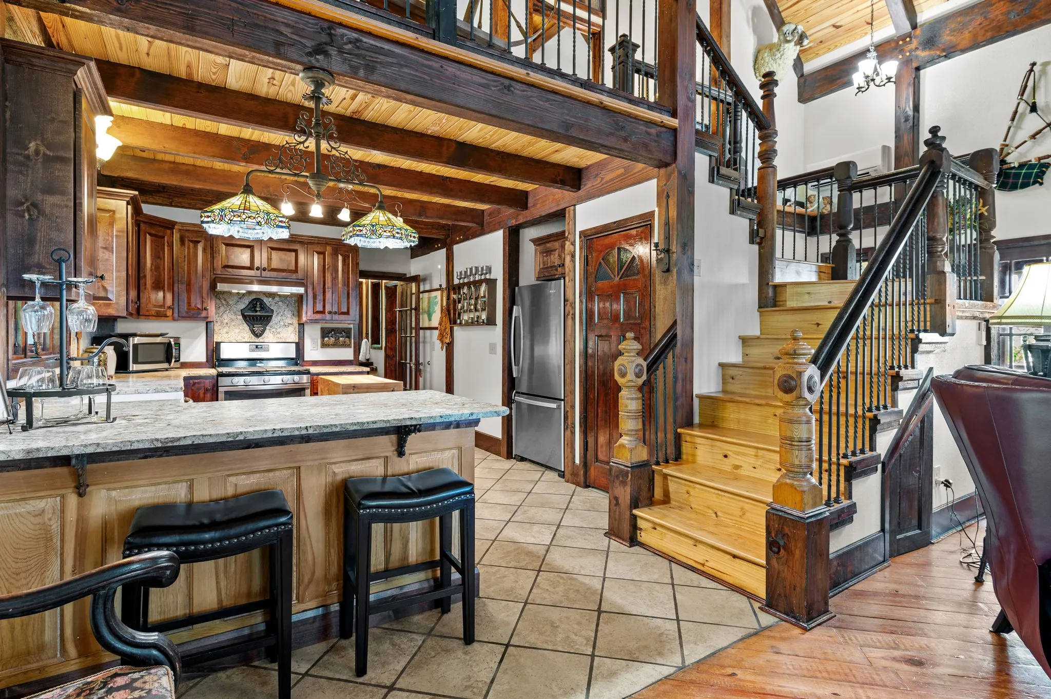 Gourmet kitchen with custom wood cabinetry, island, bar stools, and open staircase