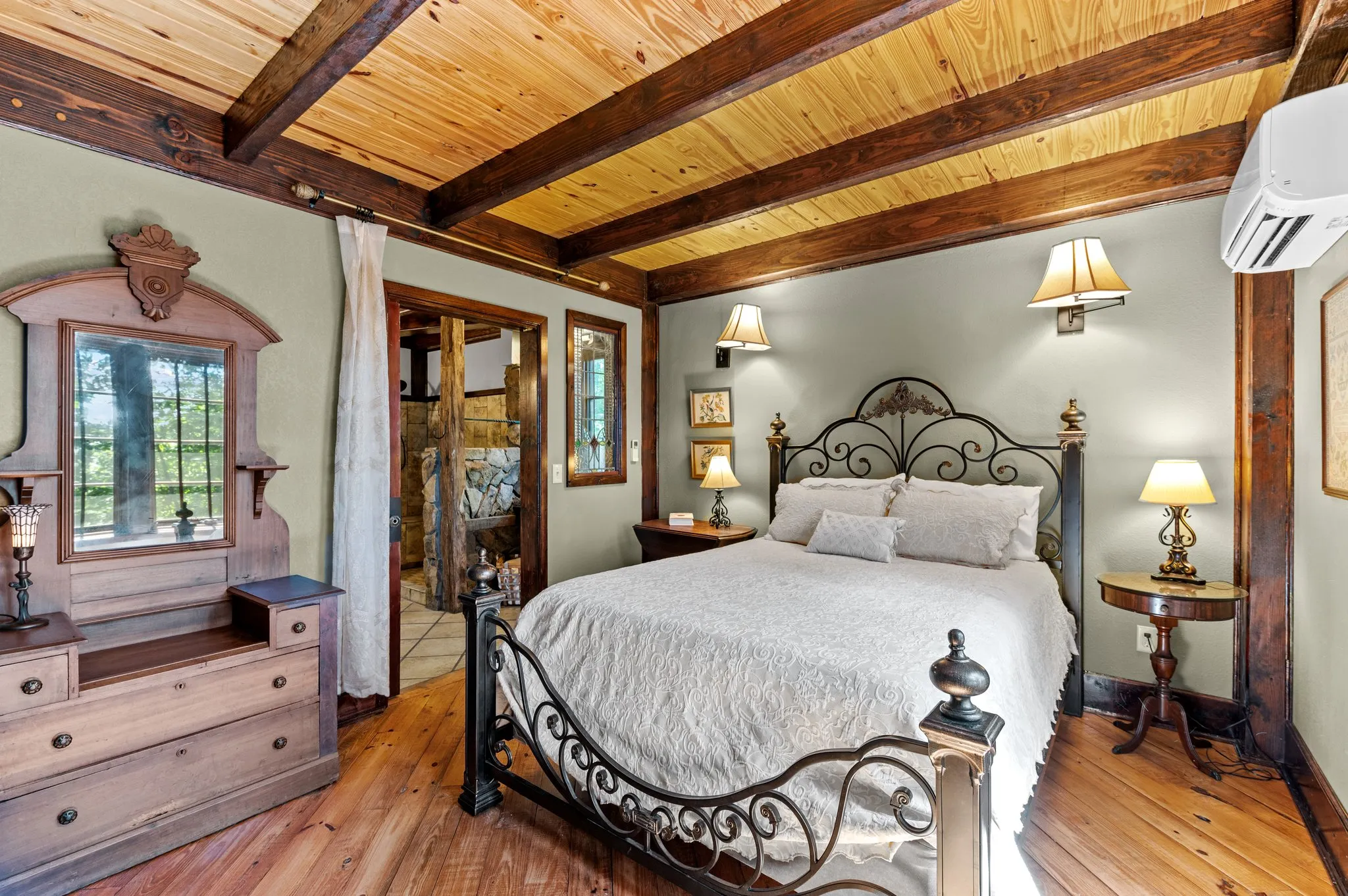 Downstairs bedroom with ornate iron bed frame, wood beams, bedside tables, and sitting area by windows
