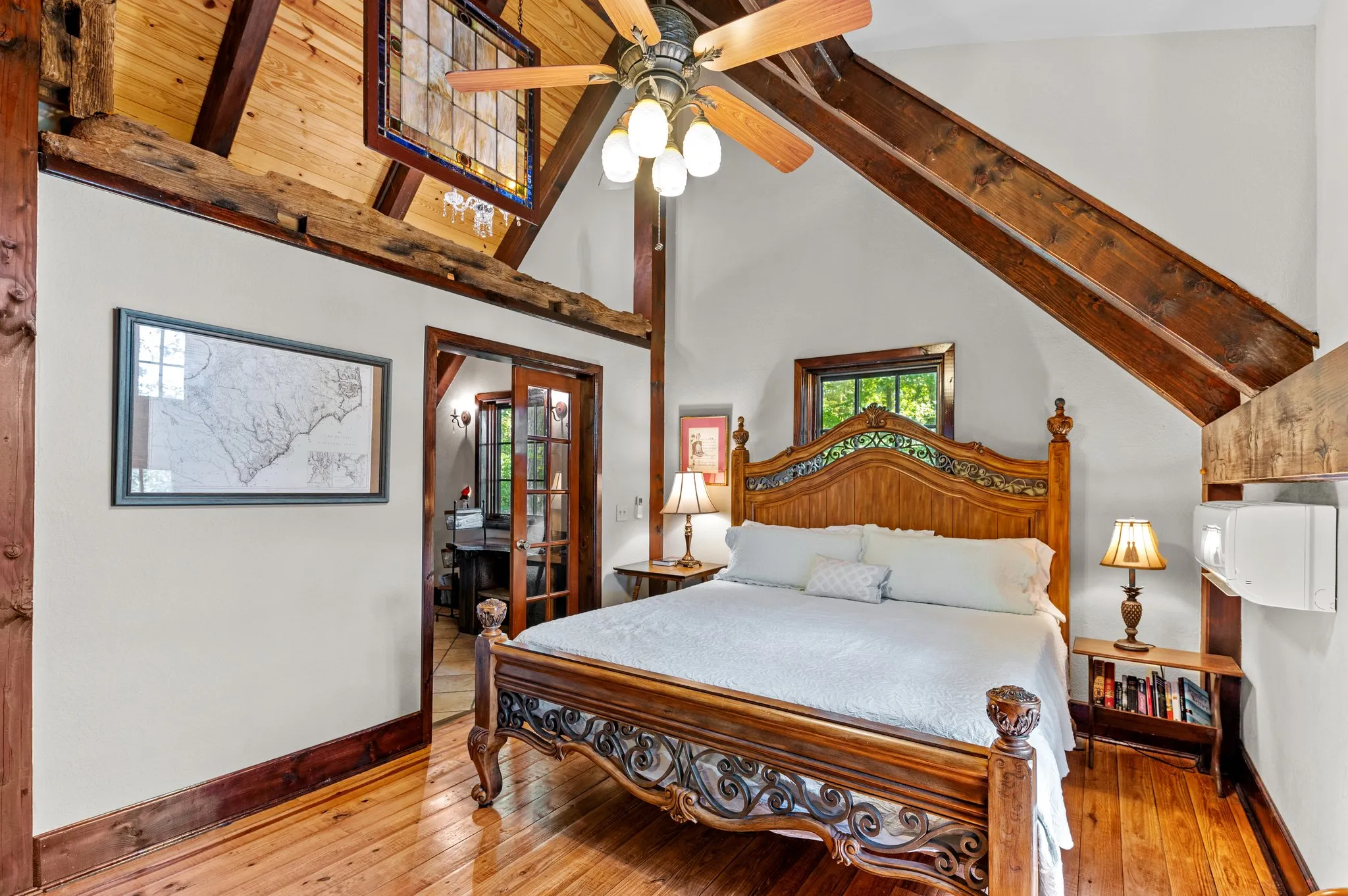 Elegant master bedroom with ornate wooden bed, high timber ceiling, ceiling fan, and natural light