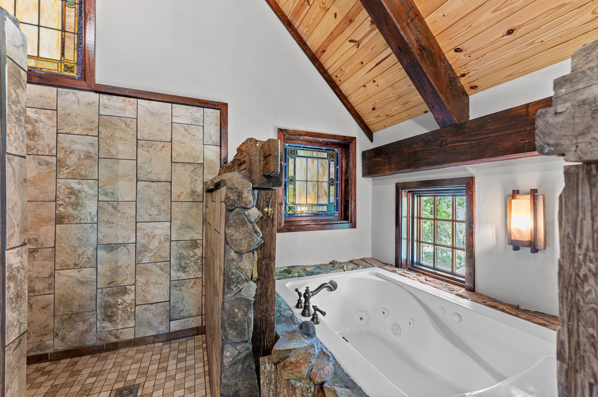 Luxurious master bathroom with jetted tub, stained glass windows, stone accents, and timber beam ceiling
