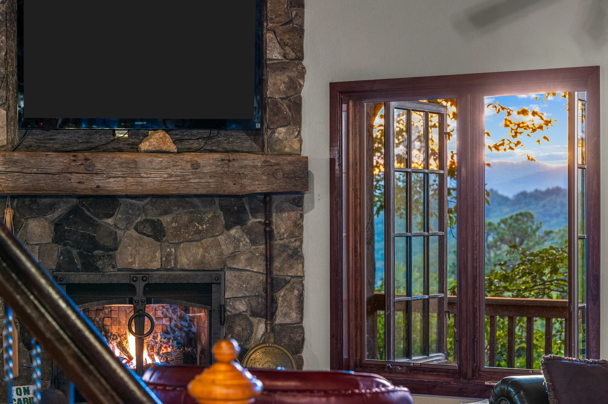 Cozy seating area with working stone fireplace, TV, and glass doors opening to panoramic mountain view