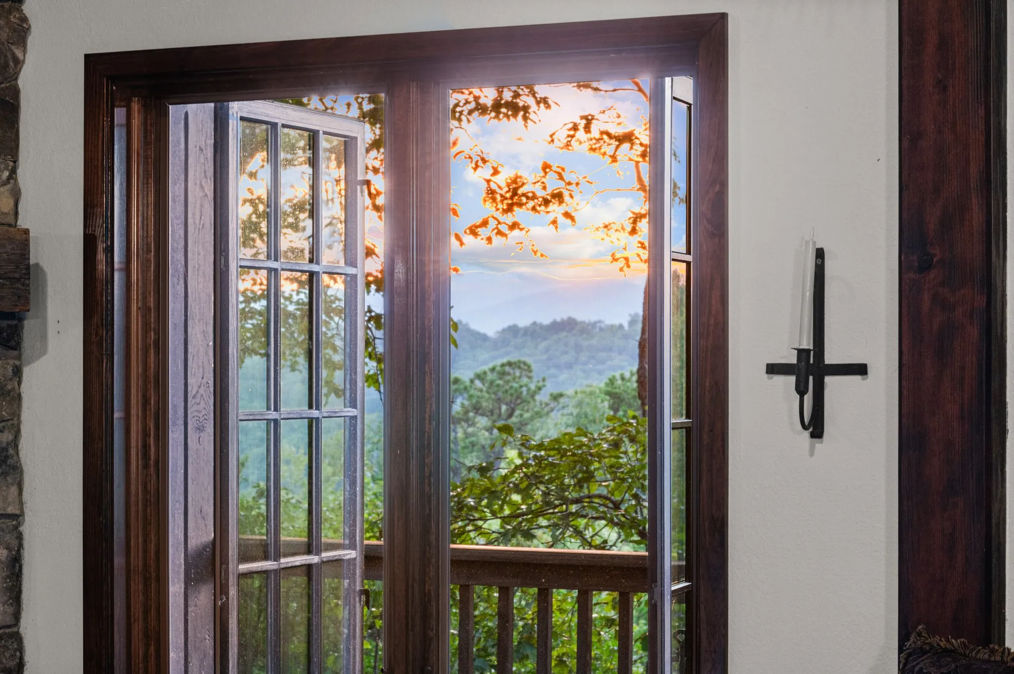 Glass doors with rustic wood frame opening onto deck overlooking mountain landscape with autumn foliage