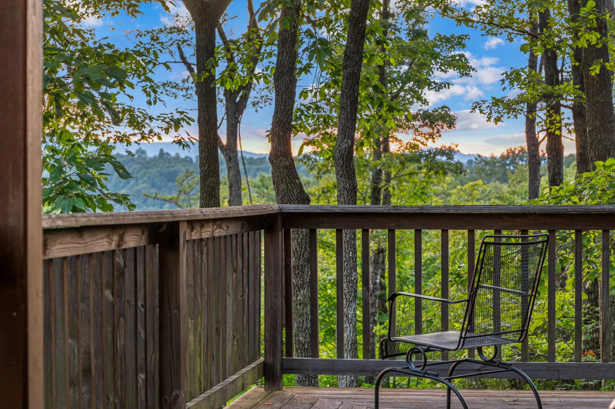 Peaceful wooden deck with chairs overlooking layered mountain ranges through forest trees