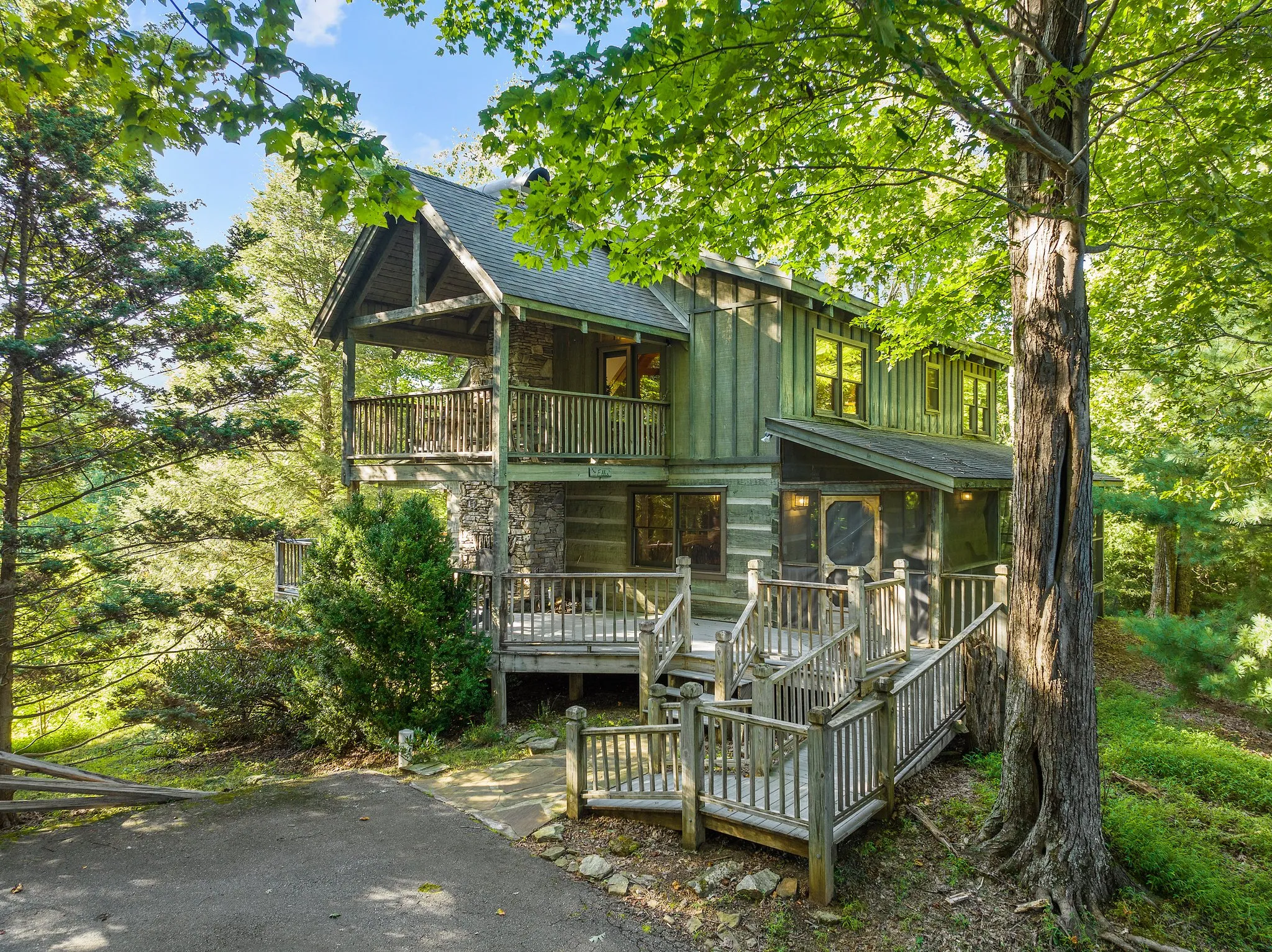 Log Cabin Front view of log cabin with stone foundation, staircase entry, and spacious upper and lower decks