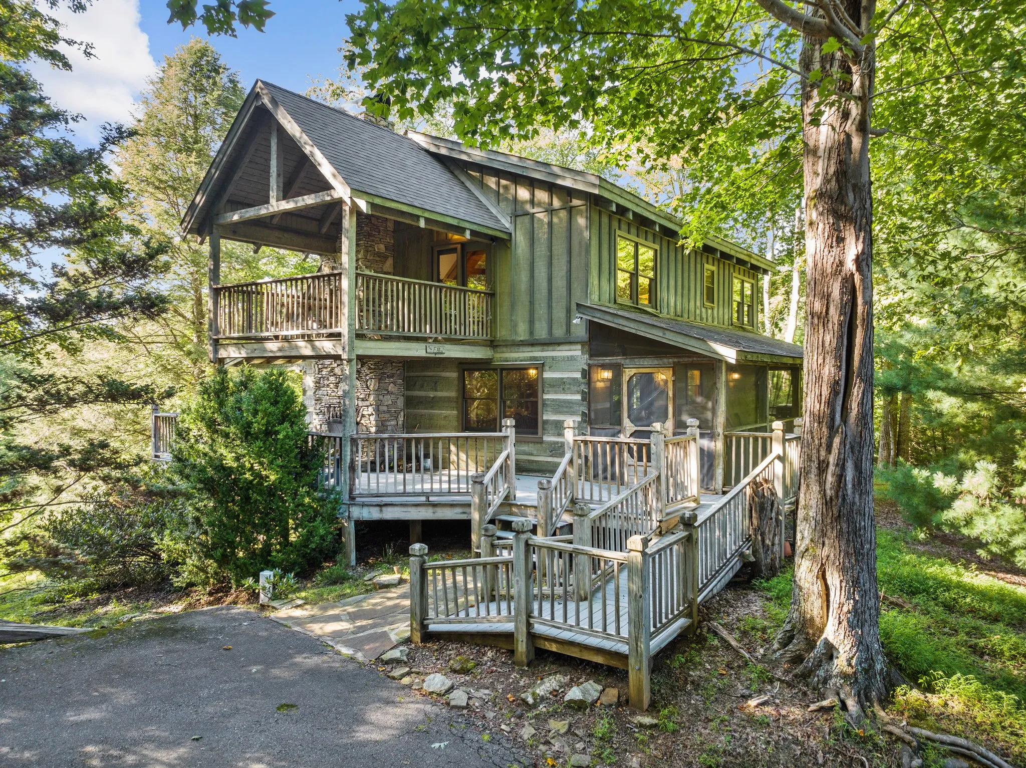 Appalachian log cabin with green metal roof, stone chimney, and multi-level wraparound decks surrounded by tall trees