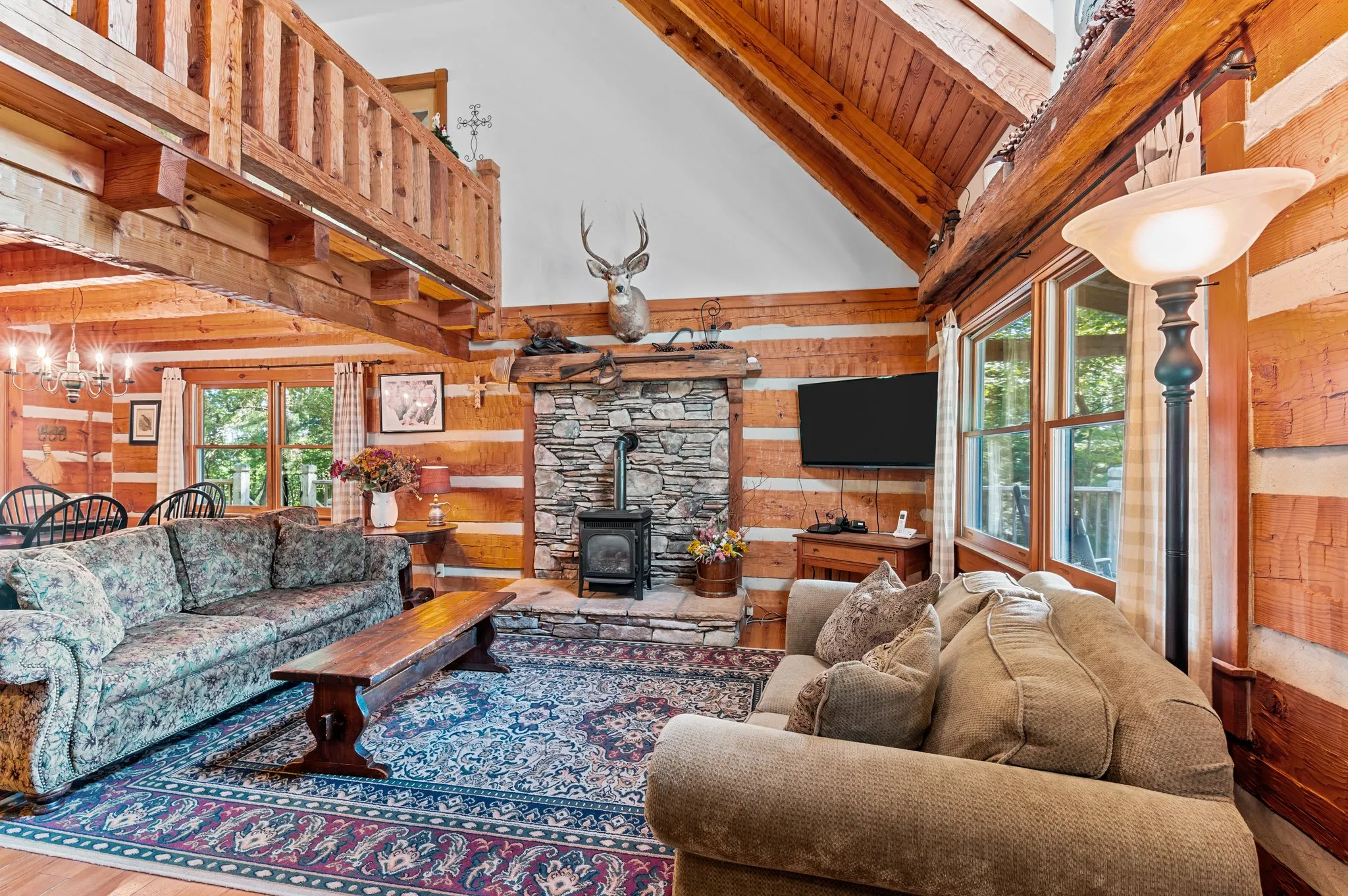Spacious great room with soaring ceiling, stone fireplace, deer mount, loft overlook, and large windows