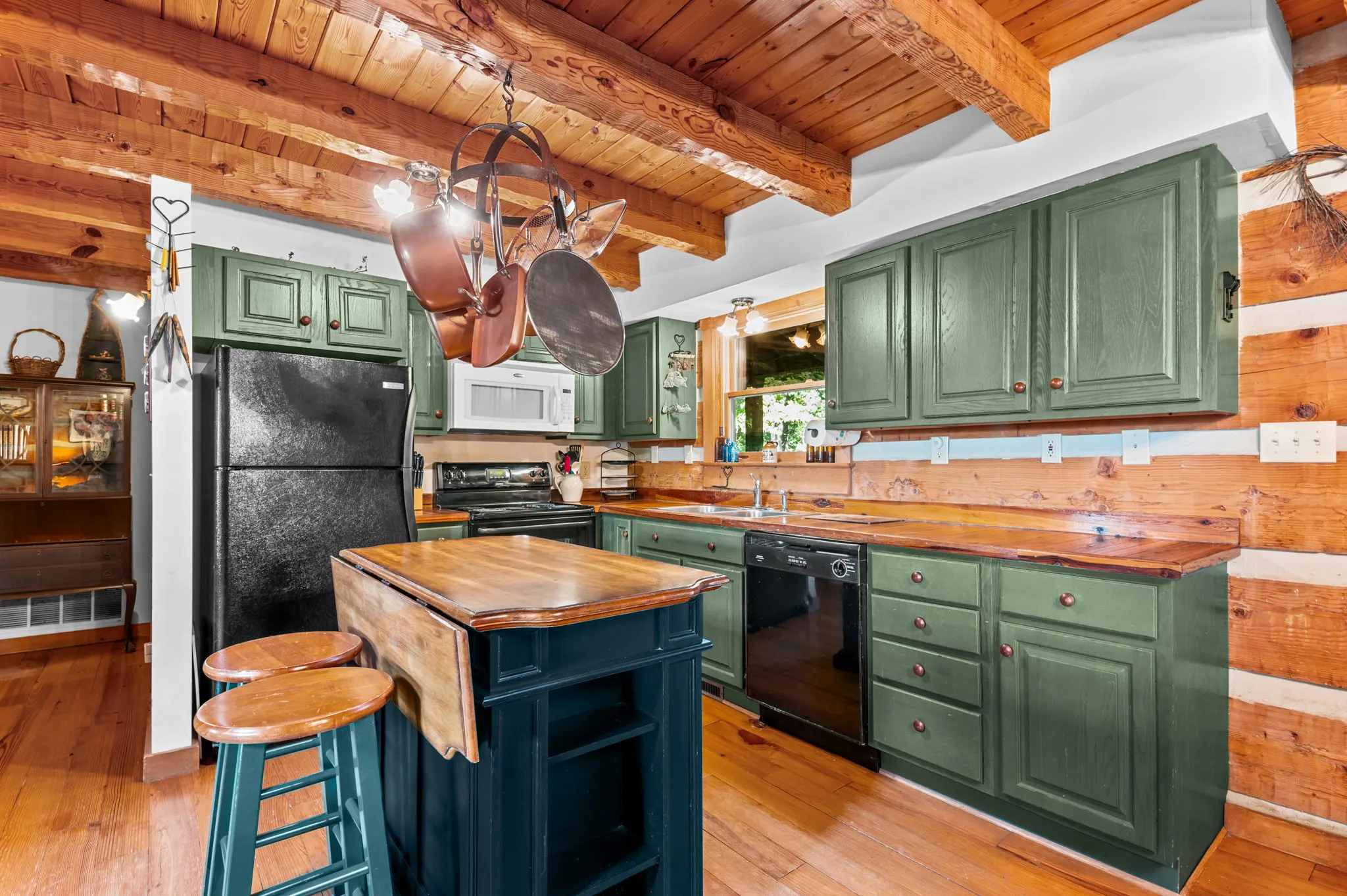 Kitchen Country kitchen with green cabinets, wood countertops, island with bar stools, and hanging pot rack