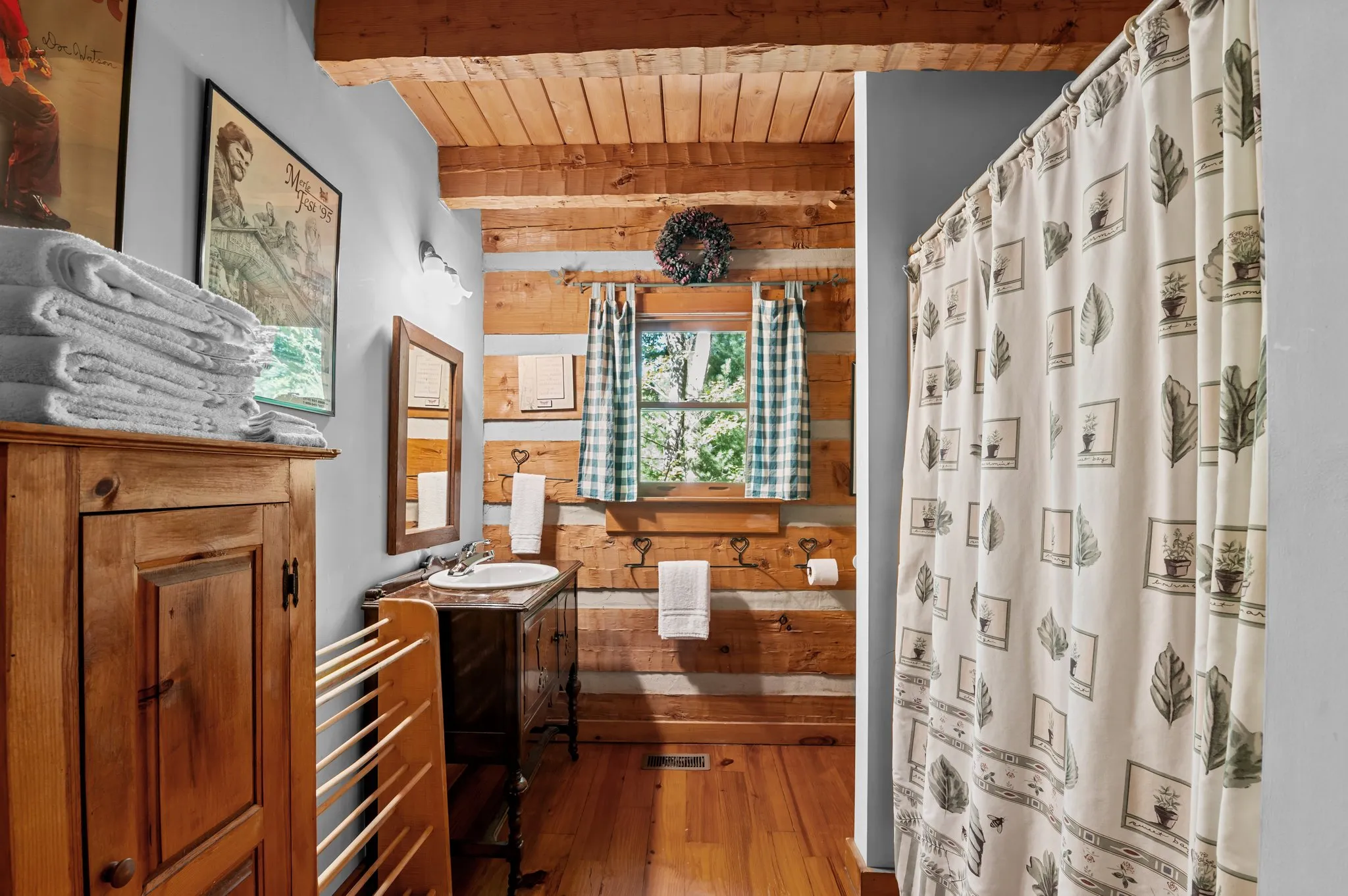Main Bathroom Rustic bathroom with log walls, pedestal sink, vintage botanical shower curtain, and stained glass window