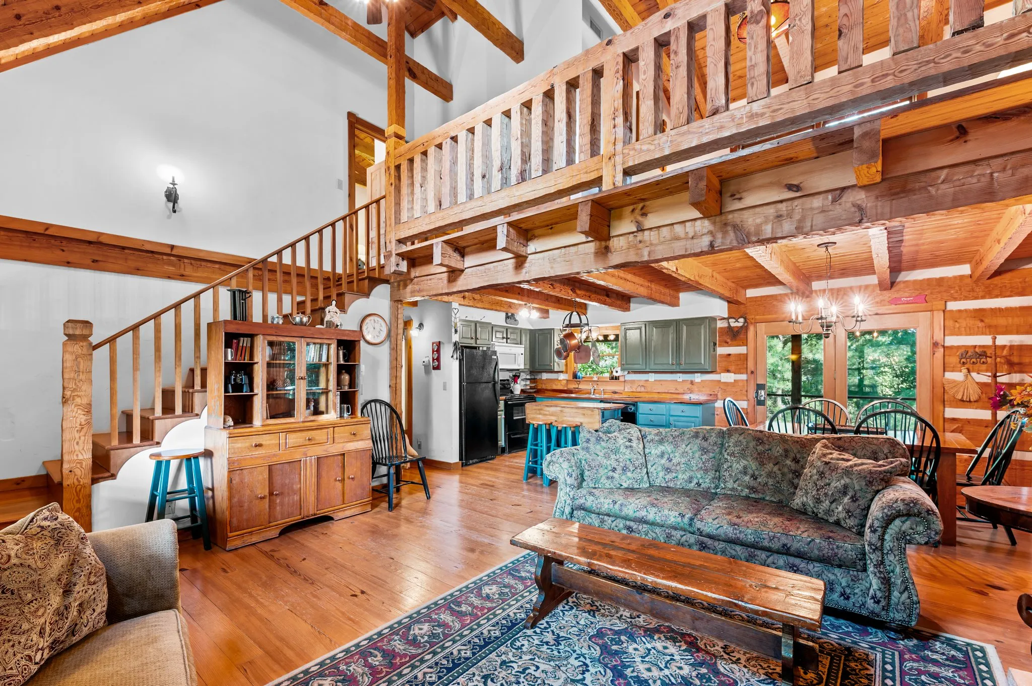Open Living Area Open concept living area showing loft staircase, green kitchen cabinets, and log beam construction