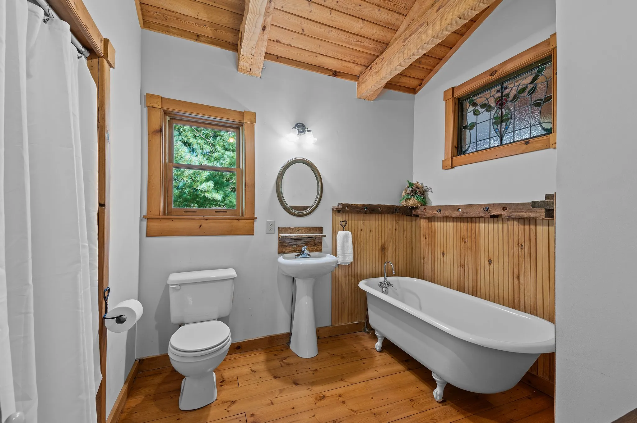 Bathroom with Clawfoot Tub Charming bathroom featuring white clawfoot tub, wood wainscoting, pedestal sink, and stained glass window