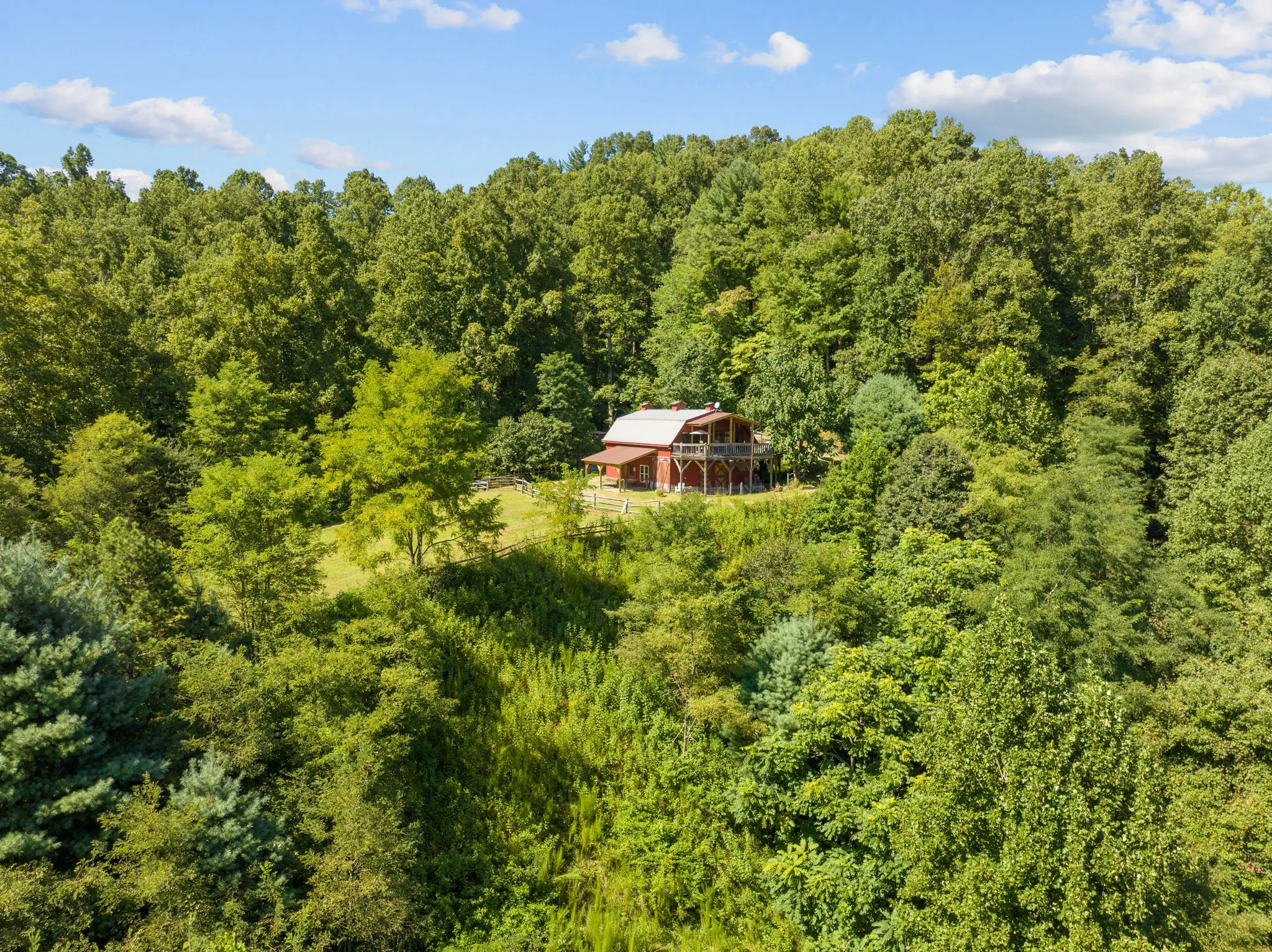 Aerial view of red barn nestled in dense mountain forest with blue sky