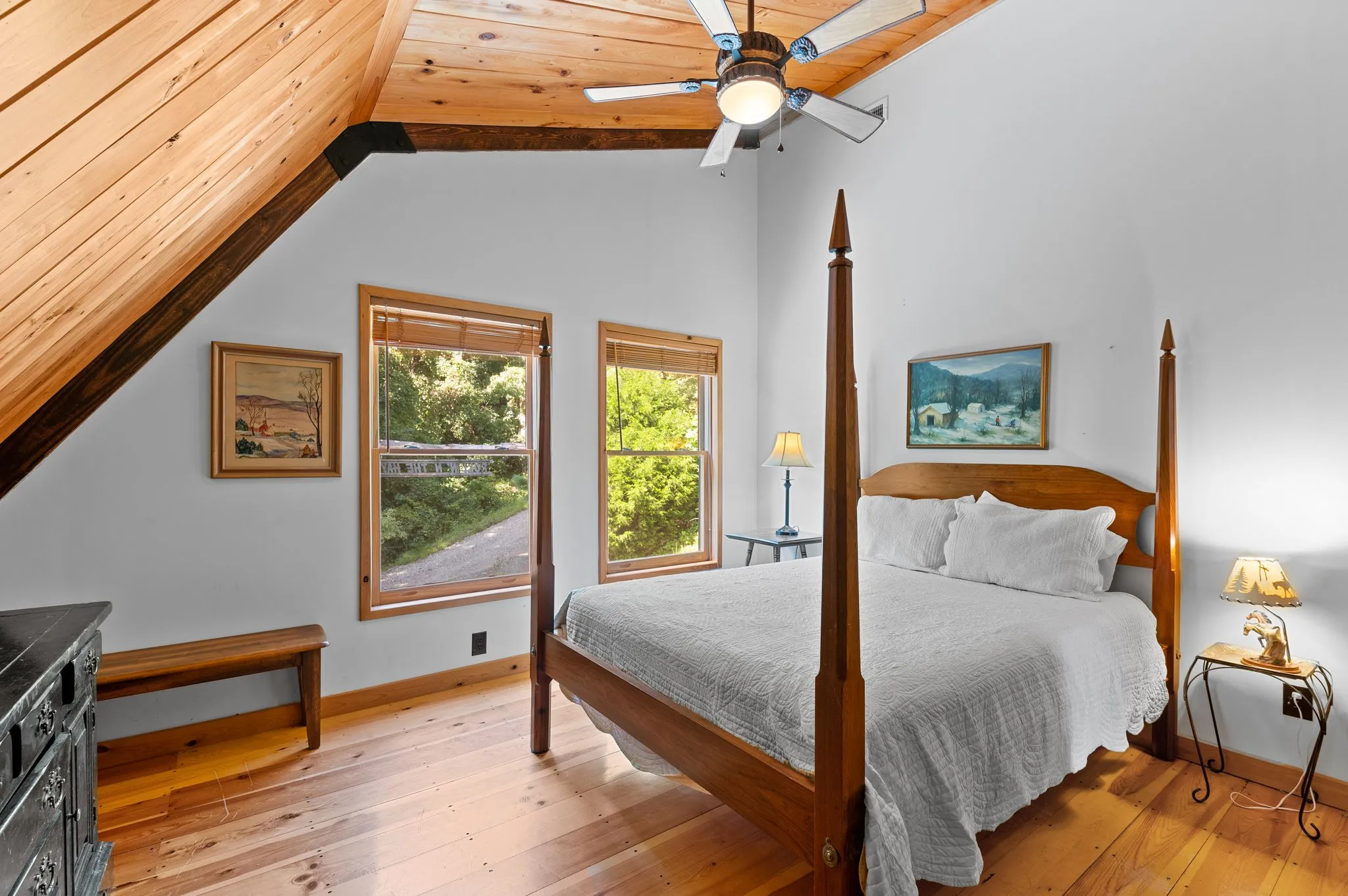 Master bedroom with vaulted wood ceiling, four-poster bed, hardwood floors, and forest views through windows