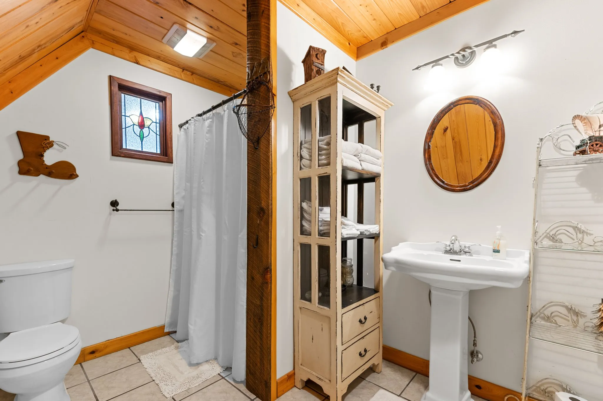 Complete bathroom view with shower curtain, pedestal sink, linen storage, and rustic barn accents