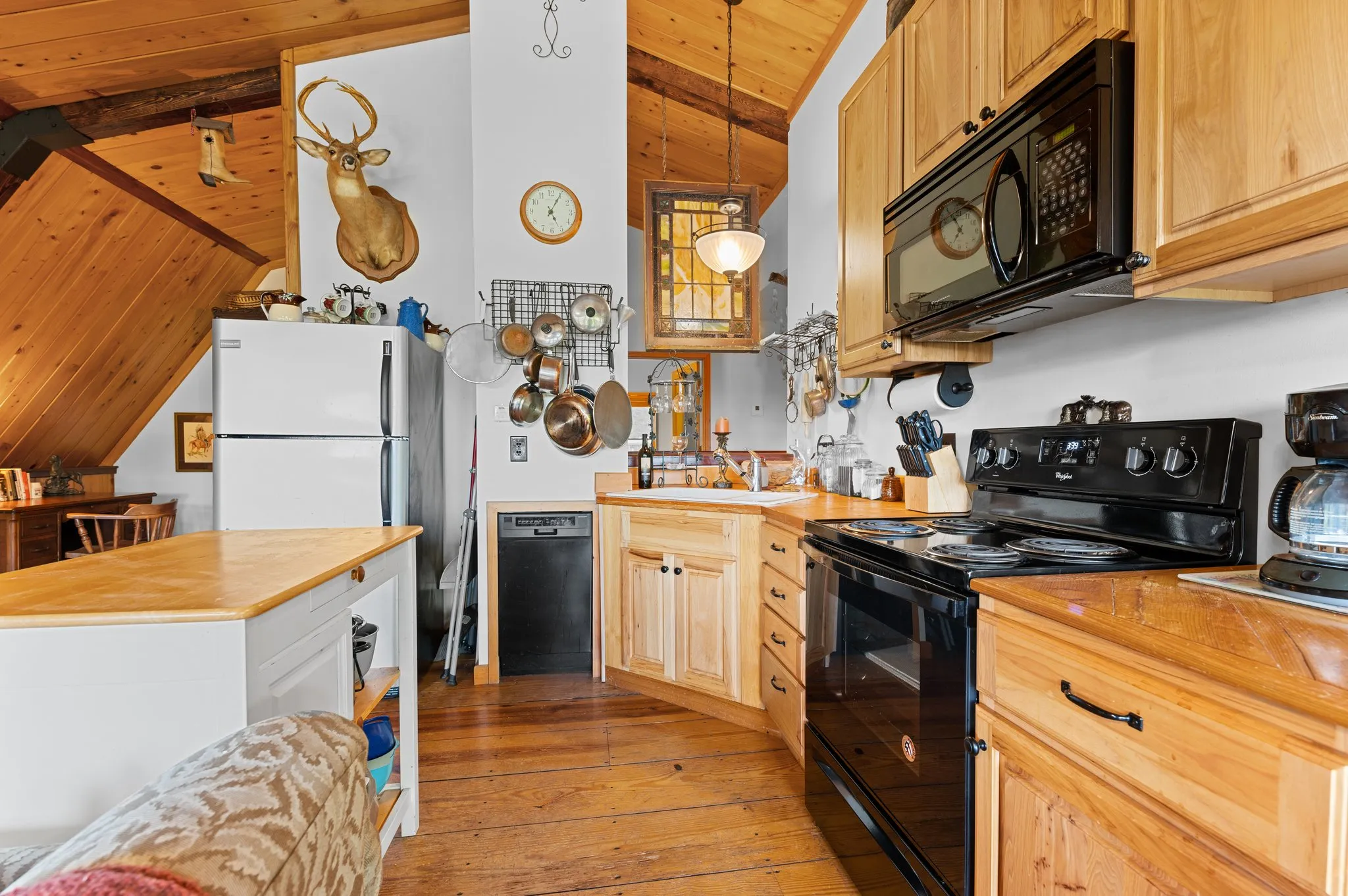 Rustic kitchen with wood cabinets, black appliances, deer mount, hanging cookware, and vaulted ceiling