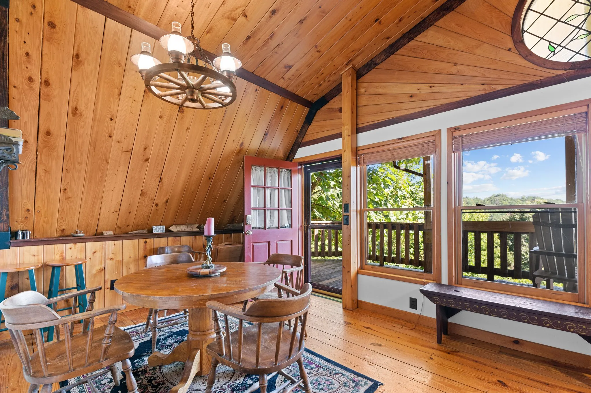 Dining space with round table, wagon wheel chandelier, pine ceiling, and picture windows overlooking deck